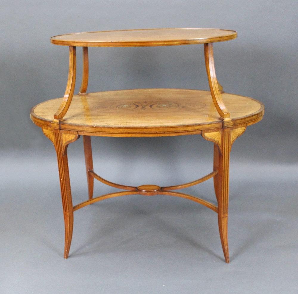 A late Victorian two-tier oval satinwood etagere table featuring central marquetry inlay, crossbanded borders, tapered legs, and swept stretchers. View II