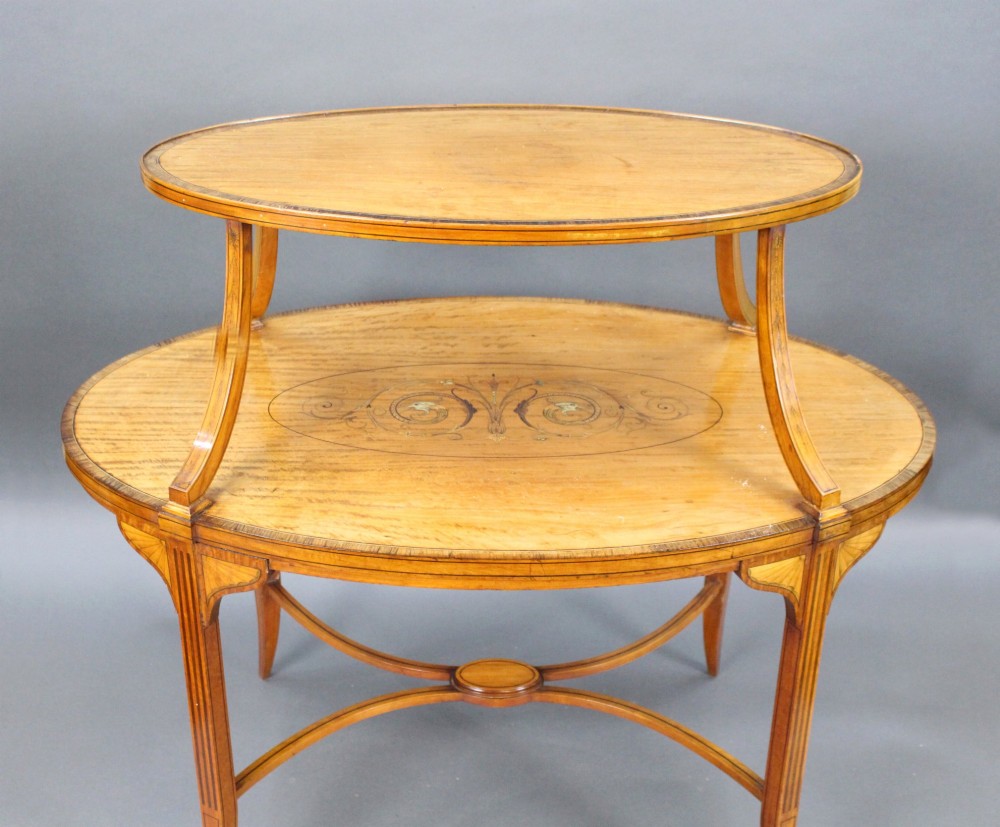 A late Victorian two-tier oval satinwood etagere table featuring central marquetry inlay, crossbanded borders, tapered legs, and swept stretchers. View III