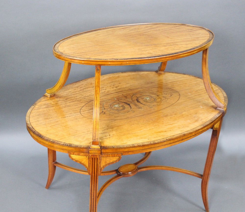 A late Victorian two-tier oval satinwood etagere table featuring central marquetry inlay, crossbanded borders, tapered legs, and swept stretchers. View IV