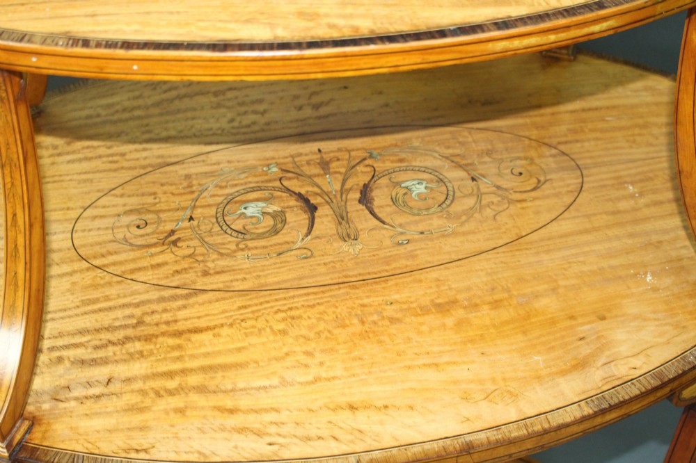 A late Victorian two-tier oval satinwood etagere table featuring central marquetry inlay, crossbanded borders, tapered legs, and swept stretchers. View V