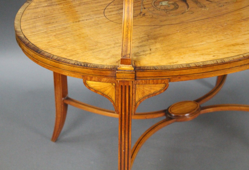 A late Victorian two-tier oval satinwood etagere table featuring central marquetry inlay, crossbanded borders, tapered legs, and swept stretchers. View VI