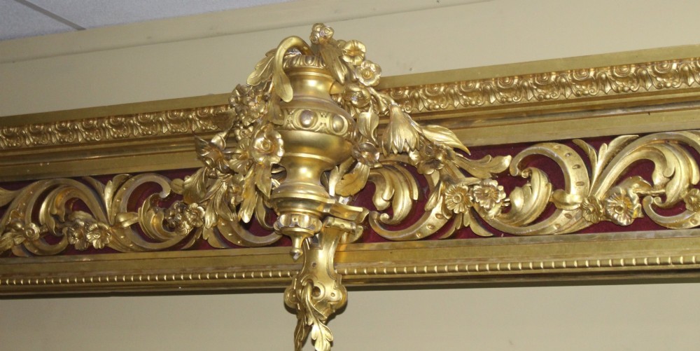 A Regency gilded wooden window pelmet featuring carved acanthus scrolls, floral swags, and a central urn motif set against a dark red fabric backing. View IV