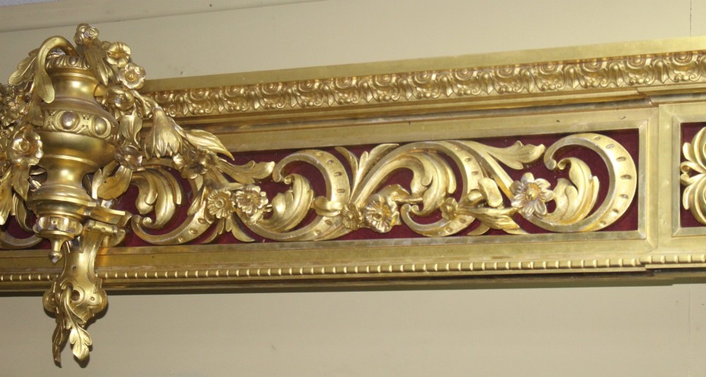 A Regency gilded wooden window pelmet featuring carved acanthus scrolls, floral swags, and a central urn motif set against a dark red fabric backing. View V