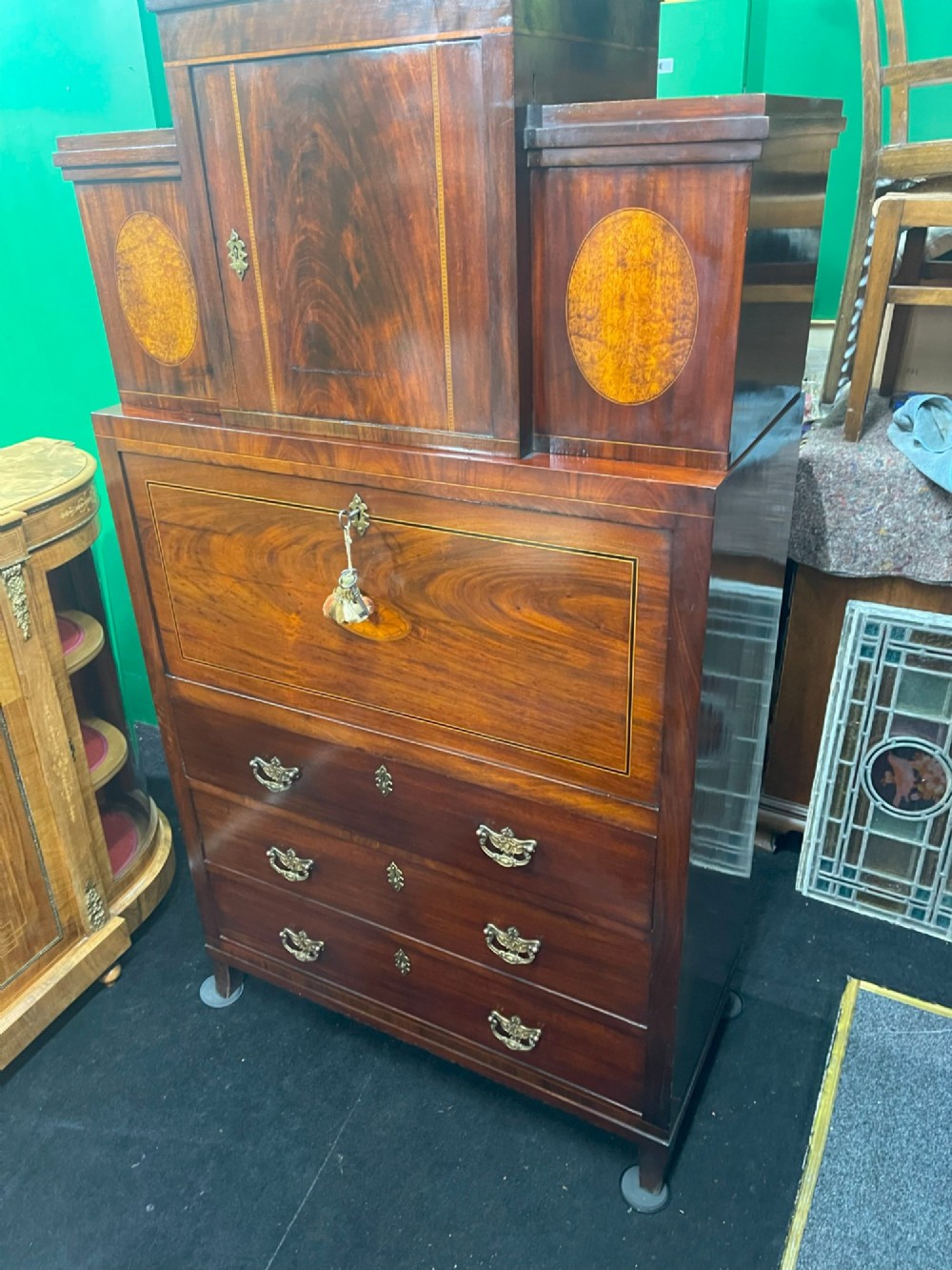 A tall Georgian mahogany secretaire chest featuring stepped upper cabinets with oval satinwood inlay, a pull-out writing drawer, and three lower drawers with brass handles. View III