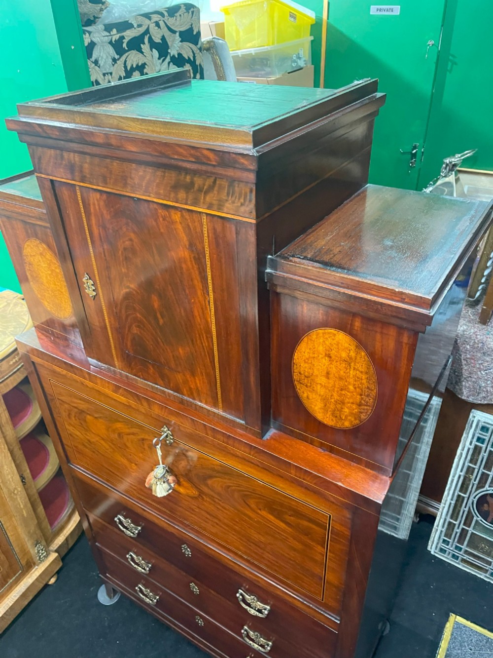 A tall Georgian mahogany secretaire chest featuring stepped upper cabinets with oval satinwood inlay, a pull-out writing drawer, and three lower drawers with brass handles. View IV