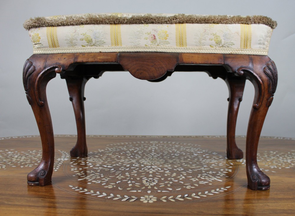 A low walnut footstool featuring carved cabriole legs and a cream and yellow floral striped fabric upholstered seat with tassel trim. View III
