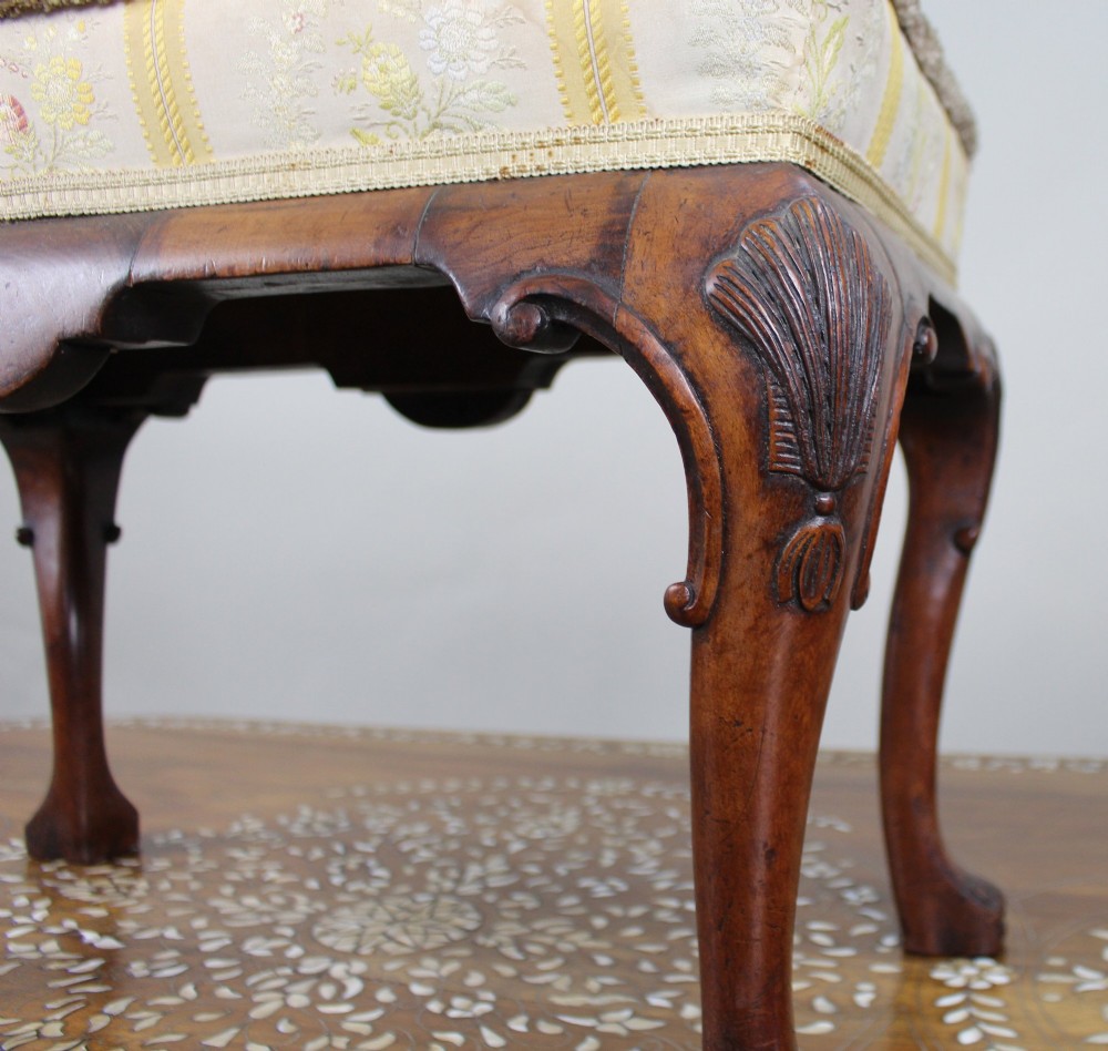 A low walnut footstool featuring carved cabriole legs and a cream and yellow floral striped fabric upholstered seat with tassel trim. View V
