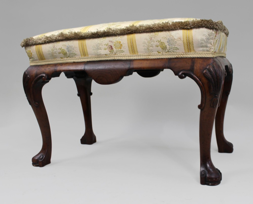 A low walnut footstool featuring carved cabriole legs and a cream and yellow floral striped fabric upholstered seat with tassel trim. View VII