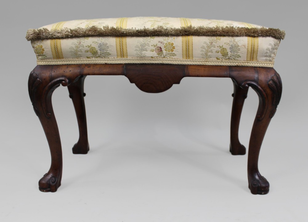 A low walnut footstool featuring carved cabriole legs and a cream and yellow floral striped fabric upholstered seat with tassel trim. View VIII