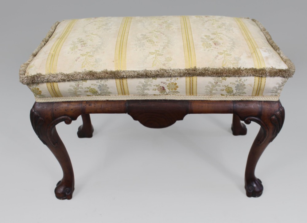 A low walnut footstool featuring carved cabriole legs and a cream and yellow floral striped fabric upholstered seat with tassel trim. View IX