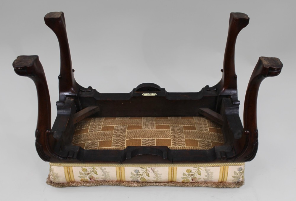 A low walnut footstool featuring carved cabriole legs and a cream and yellow floral striped fabric upholstered seat with tassel trim. View XI