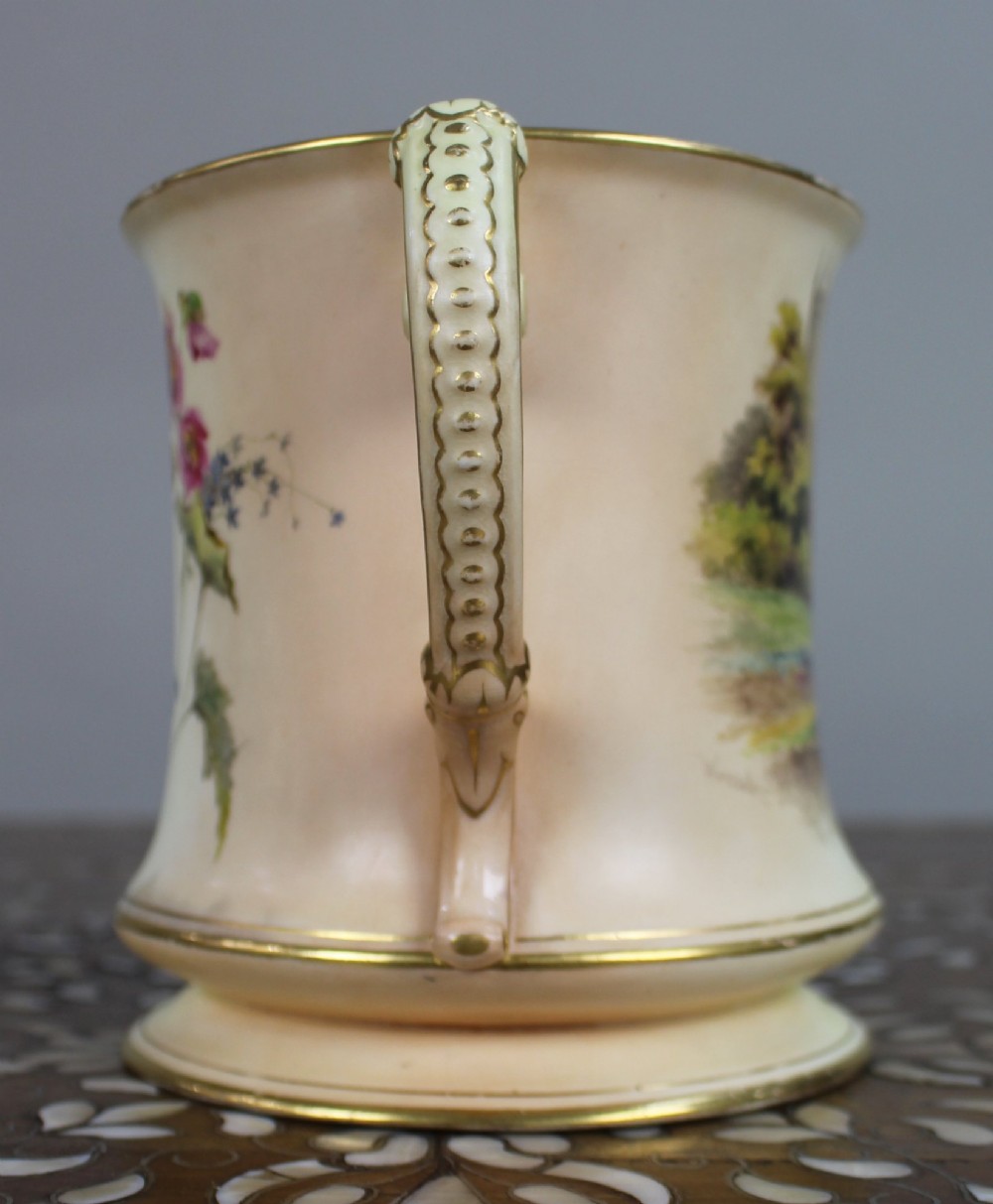An Edwardian Royal Worcester porcelain loving cup featuring twin gilded scroll handles, a cream blush ground, hand-painted floral motifs, and a central gilt monogram. View IV