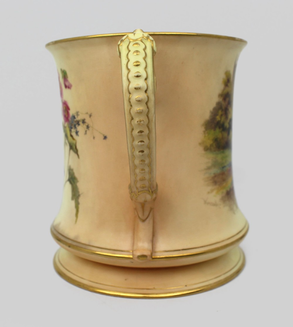 An Edwardian Royal Worcester porcelain loving cup featuring twin gilded scroll handles, a cream blush ground, hand-painted floral motifs, and a central gilt monogram. View IX