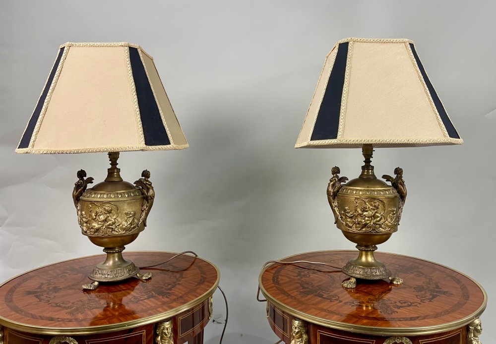 A pair of antique French gilt bronze urn-form table lamps decorated with putti reliefs and fitted with neutral fabric shades. View II