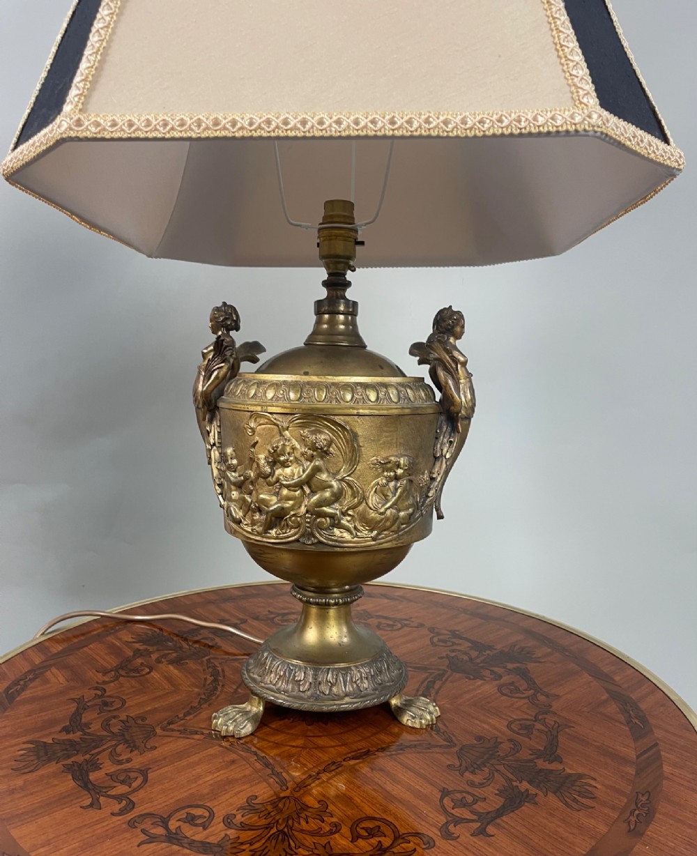 A pair of antique French gilt bronze urn-form table lamps decorated with putti reliefs and fitted with neutral fabric shades. View V