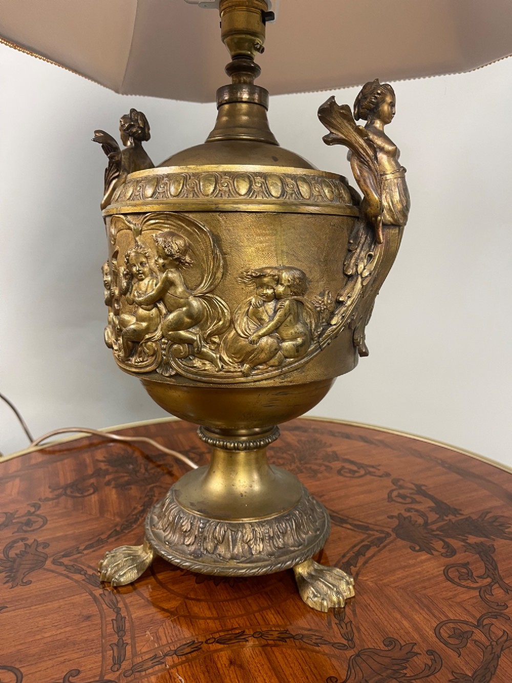 A pair of antique French gilt bronze urn-form table lamps decorated with putti reliefs and fitted with neutral fabric shades. View VIII