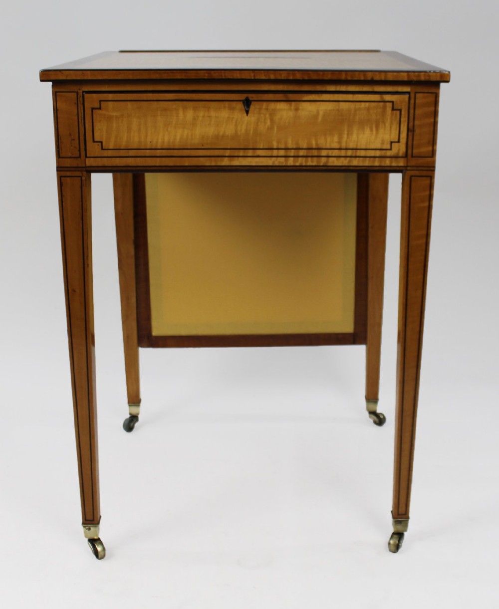 A George III Sheraton satinwood writing table featuring dark wood crossbanding, line inlay, a single drawer, square tapered legs, and brass castors. View V