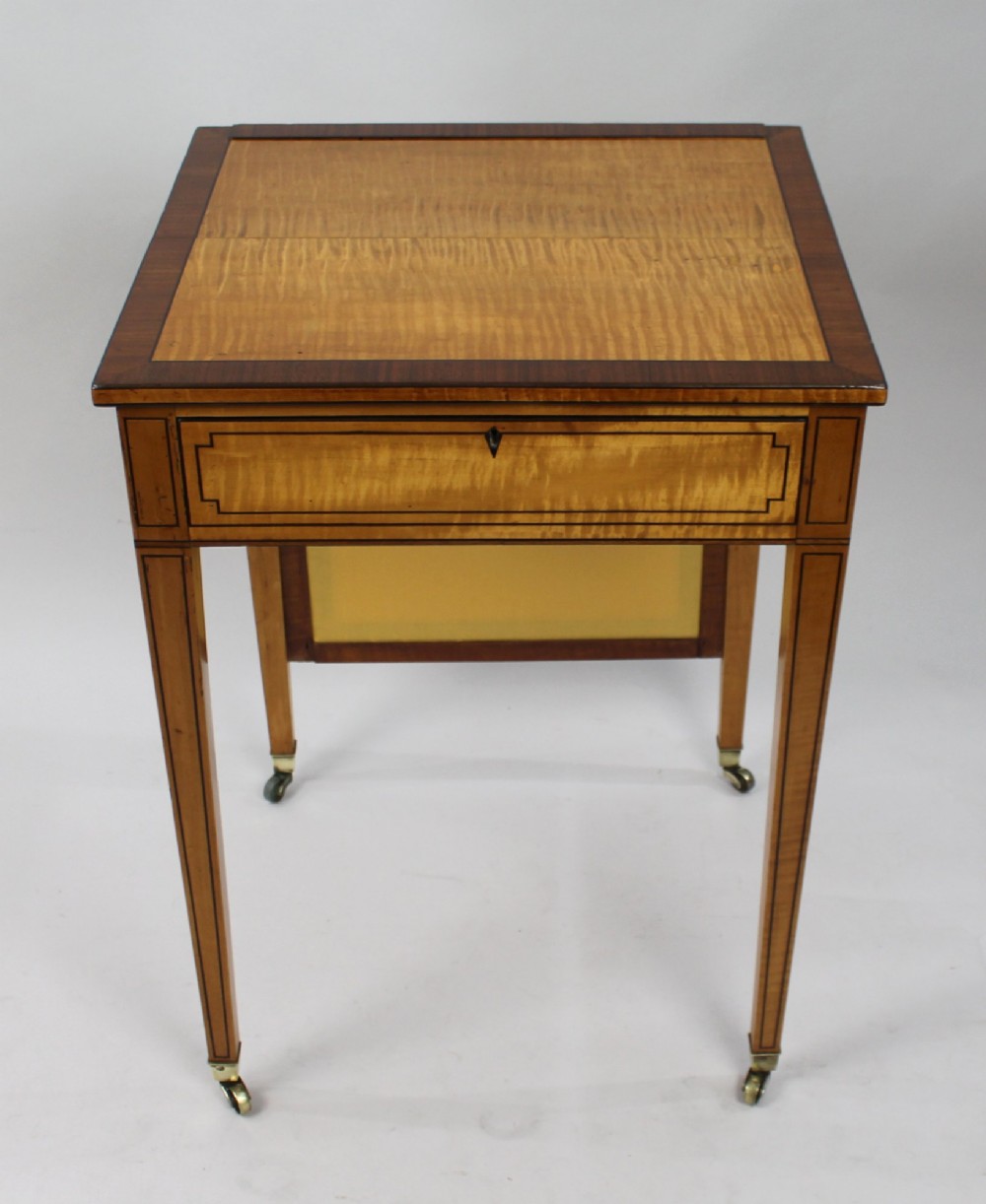 A George III Sheraton satinwood writing table featuring dark wood crossbanding, line inlay, a single drawer, square tapered legs, and brass castors. View VI