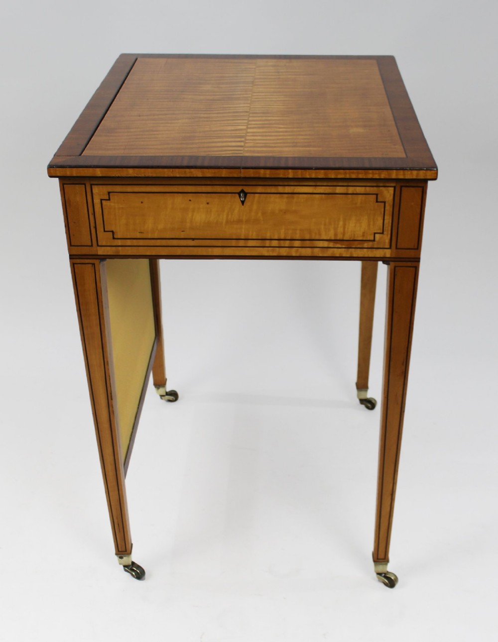 A George III Sheraton satinwood writing table featuring dark wood crossbanding, line inlay, a single drawer, square tapered legs, and brass castors. View VIII
