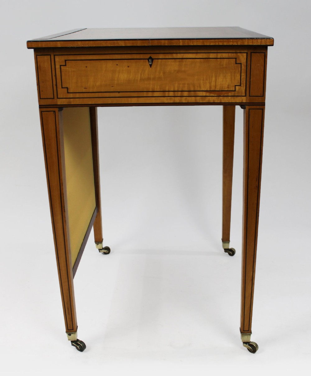 A George III Sheraton satinwood writing table featuring dark wood crossbanding, line inlay, a single drawer, square tapered legs, and brass castors. View IX