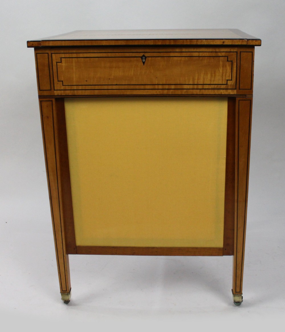 A George III Sheraton satinwood writing table featuring dark wood crossbanding, line inlay, a single drawer, square tapered legs, and brass castors. View X