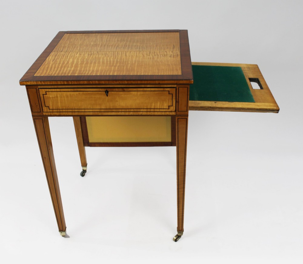 A George III Sheraton satinwood writing table featuring dark wood crossbanding, line inlay, a single drawer, square tapered legs, and brass castors. View XII