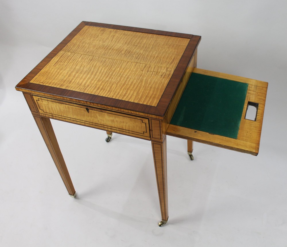 A George III Sheraton satinwood writing table featuring dark wood crossbanding, line inlay, a single drawer, square tapered legs, and brass castors. View XIII