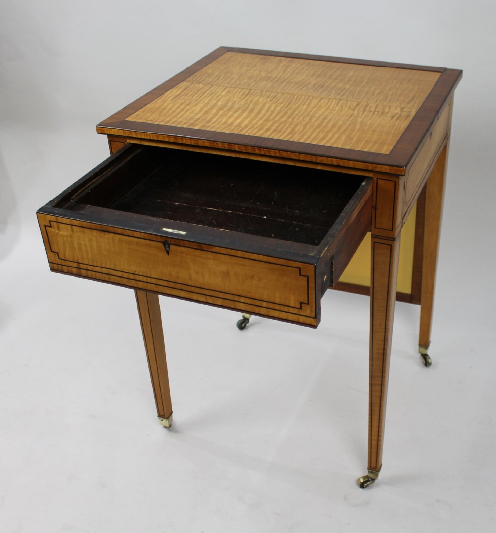 A George III Sheraton satinwood writing table featuring dark wood crossbanding, line inlay, a single drawer, square tapered legs, and brass castors. View XIV