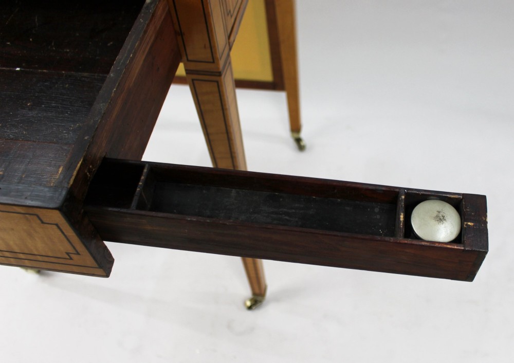 A George III Sheraton satinwood writing table featuring dark wood crossbanding, line inlay, a single drawer, square tapered legs, and brass castors. View XV