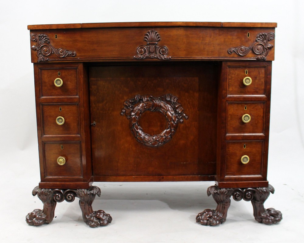 A George III mahogany work table featuring carved lion paw feet, a central door with a carved wreath, flanking side drawers, and brass knob handles. View III