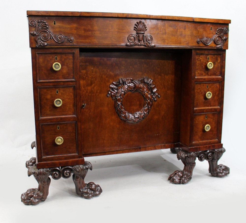 A George III mahogany work table featuring carved lion paw feet, a central door with a carved wreath, flanking side drawers, and brass knob handles. View IV