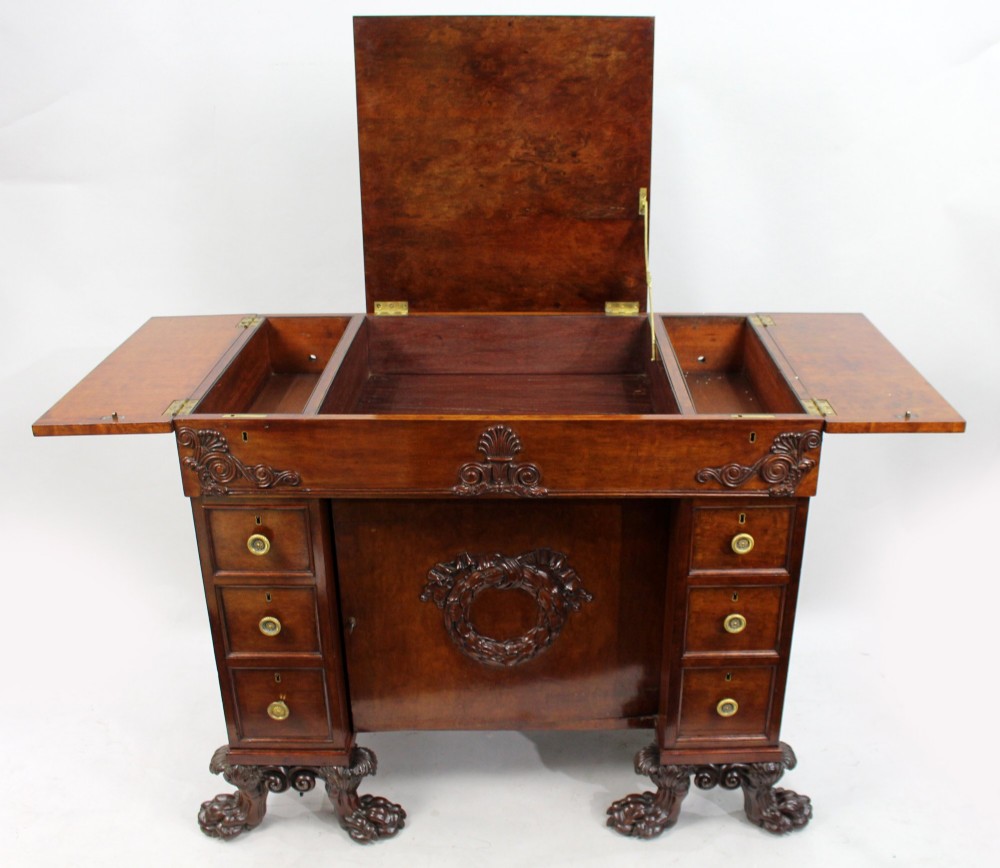 A George III mahogany work table featuring carved lion paw feet, a central door with a carved wreath, flanking side drawers, and brass knob handles. View VI