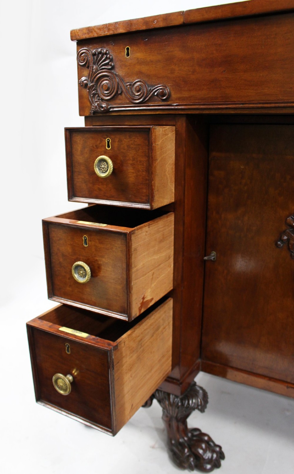 A George III mahogany work table featuring carved lion paw feet, a central door with a carved wreath, flanking side drawers, and brass knob handles. View XI