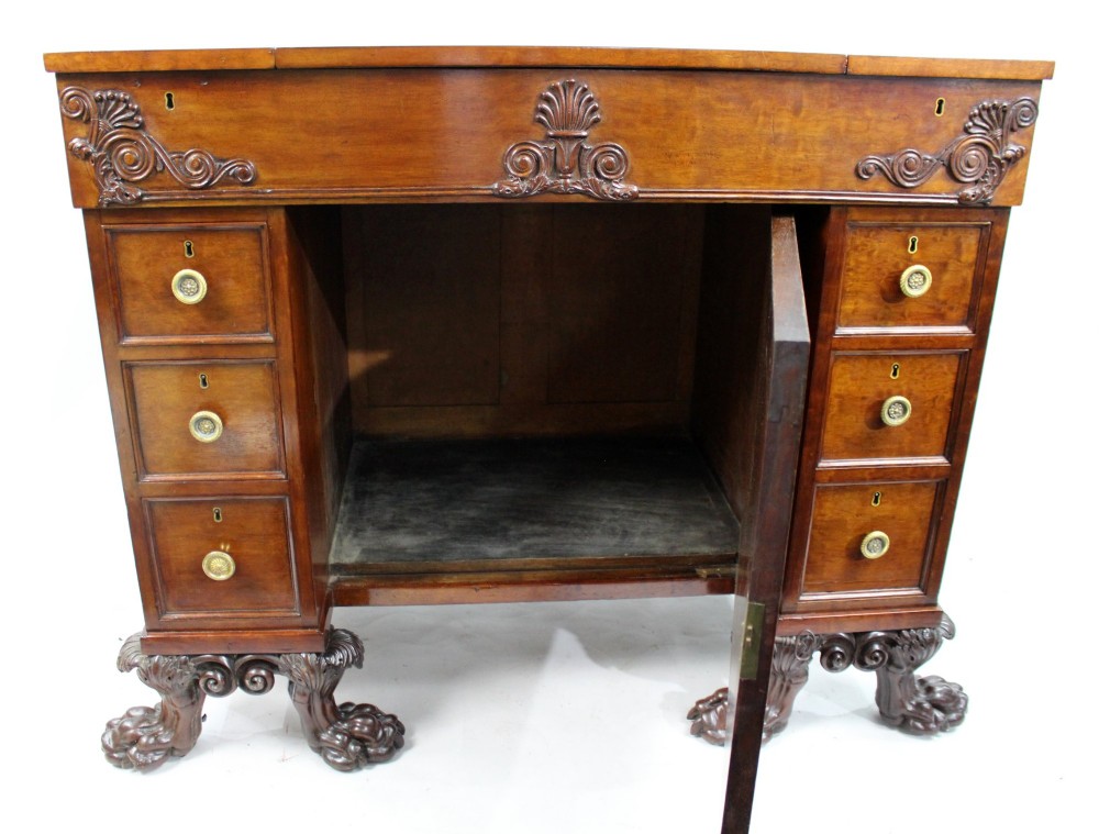 A George III mahogany work table featuring carved lion paw feet, a central door with a carved wreath, flanking side drawers, and brass knob handles. View XII