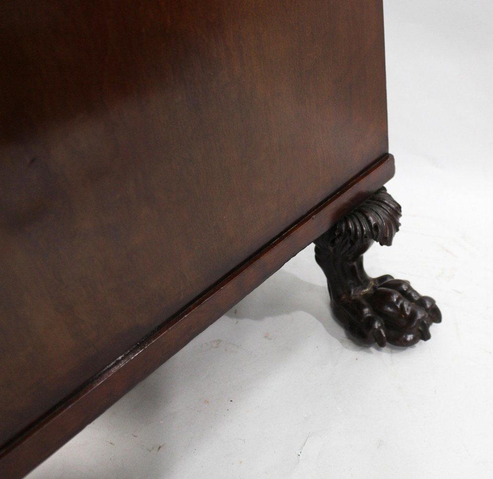 A George III mahogany work table featuring carved lion paw feet, a central door with a carved wreath, flanking side drawers, and brass knob handles. View XIV