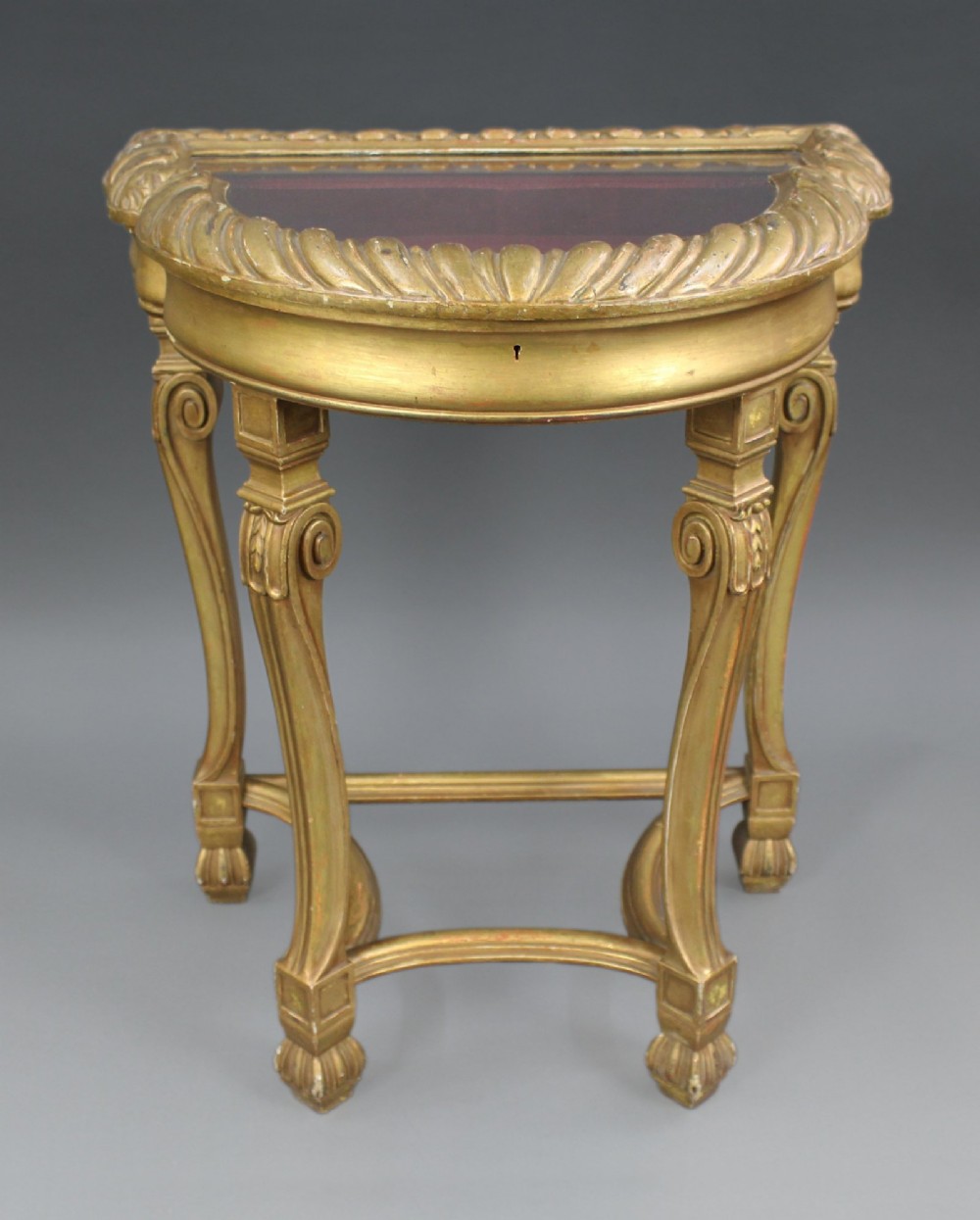 A French Louis XV Revival style giltwood demilune bijouterie table with a glass top, gadrooned rim, cabriole legs, and a velvet-lined display interior.
