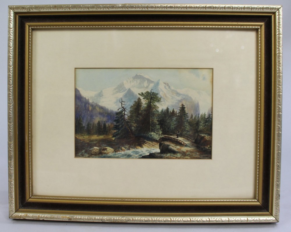 A framed watercolour painting depicting snow-capped alpine mountains behind evergreen trees and a small wooden bridge over a stream, presented in a dark mount and gilt frame.