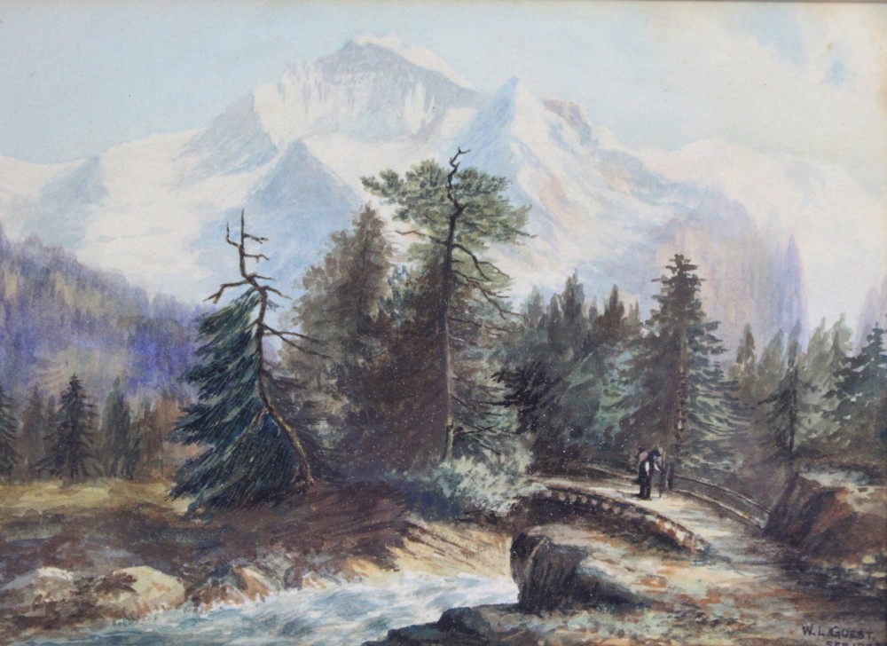 A framed watercolour painting depicting snow-capped alpine mountains behind evergreen trees and a small wooden bridge over a stream, presented in a dark mount and gilt frame. View II