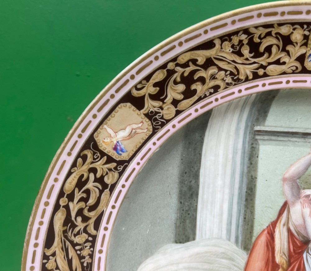 A circular 19th-century Meissen porcelain cabinet plate featuring a central hand-painted classical scene framed by a dark burgundy rim with intricate gilded scrollwork and cherub cartouches. View VIII