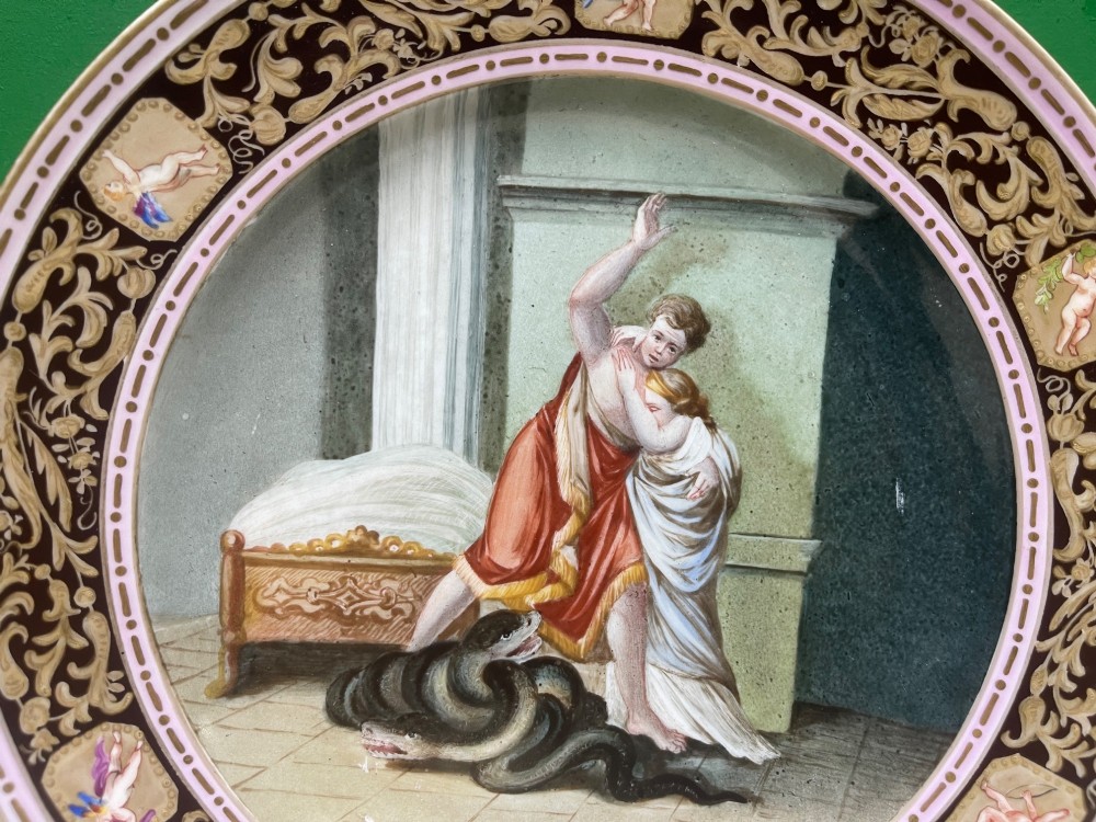 A circular 19th-century Meissen porcelain cabinet plate featuring a central hand-painted classical scene framed by a dark burgundy rim with intricate gilded scrollwork and cherub cartouches. View IX