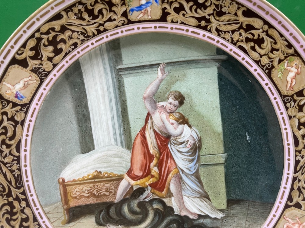 A circular 19th-century Meissen porcelain cabinet plate featuring a central hand-painted classical scene framed by a dark burgundy rim with intricate gilded scrollwork and cherub cartouches. View XI