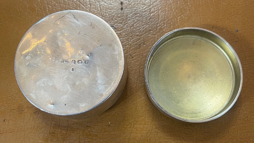 A circular Edwardian silver box lid featuring a blue engine-turned guilloche enamel centre surrounded by a white enamel border with green foliage and dark grape motifs. View IV