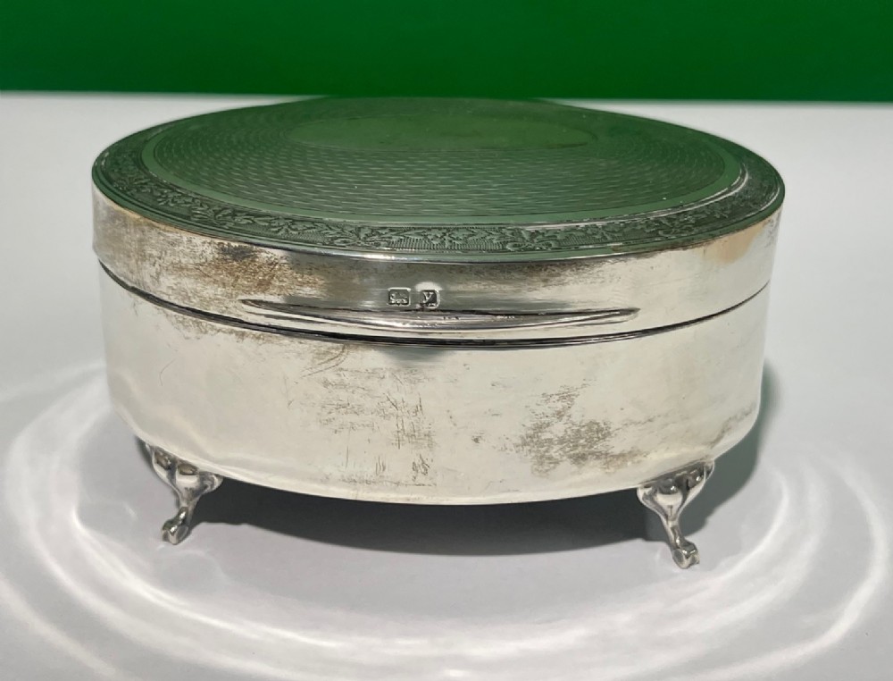 An oval sterling silver footed trinket casket featuring an engine-turned top, floral engraved lid border, and four scroll feet. View VI
