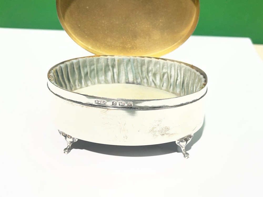 An oval sterling silver footed trinket casket featuring an engine-turned top, floral engraved lid border, and four scroll feet. View VII