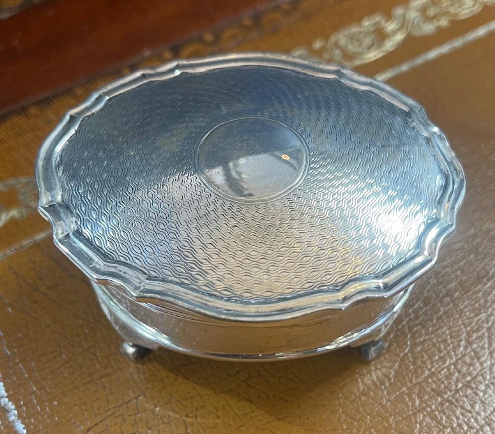 An oval sterling silver trinket box featuring an engine-turned wave pattern on the lid and resting on four small feet.