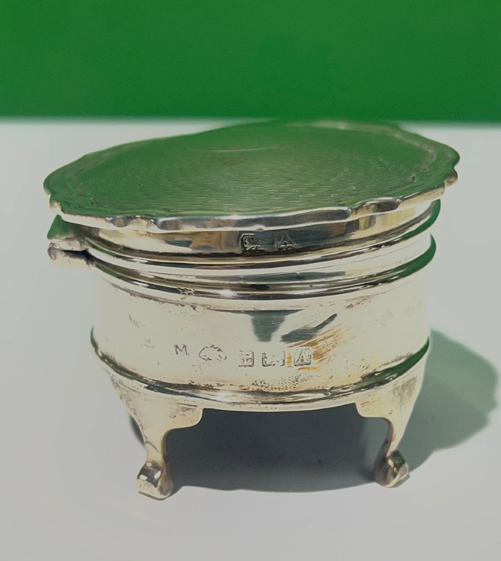 An oval sterling silver trinket box featuring an engine-turned wave pattern on the lid and resting on four small feet. View VI