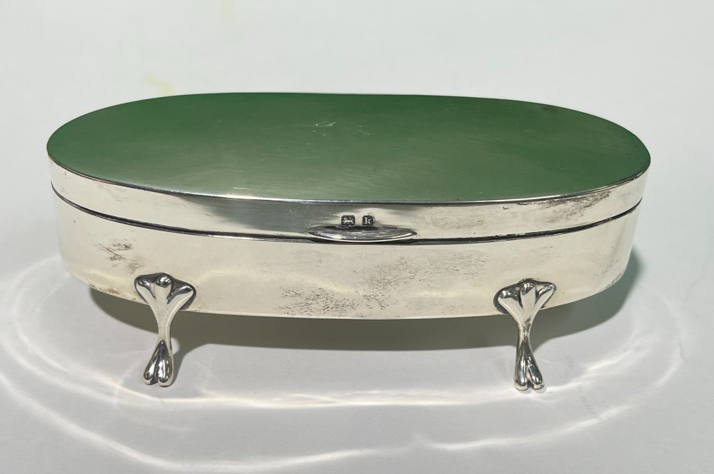 An oval sterling silver casket featuring a hinged lid, smooth polished exterior, raised cabriole feet, and visible British hallmarks.