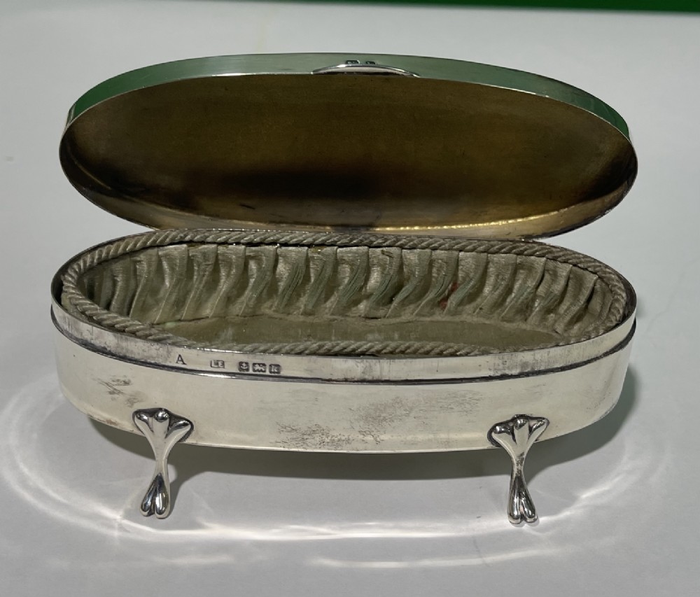 An oval sterling silver casket featuring a hinged lid, smooth polished exterior, raised cabriole feet, and visible British hallmarks. View II