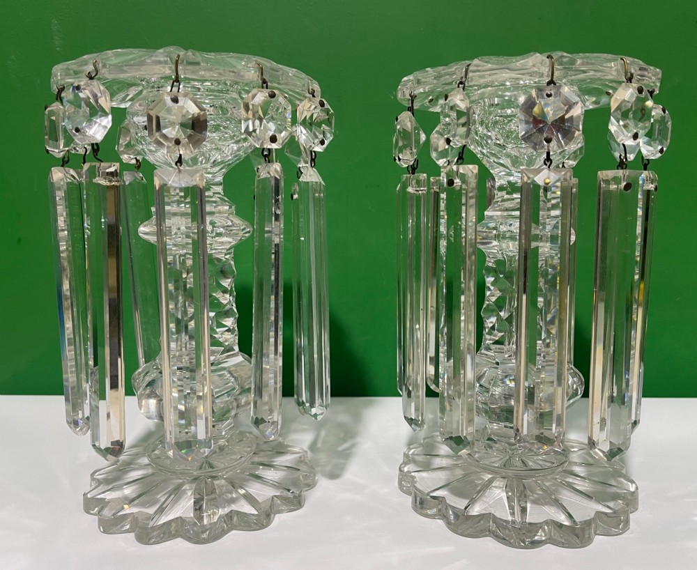 A pair of clear cut glass table lustres featuring faceted stems, starburst cut bases, and hanging crystal prism drops suspended from wire hooks.
