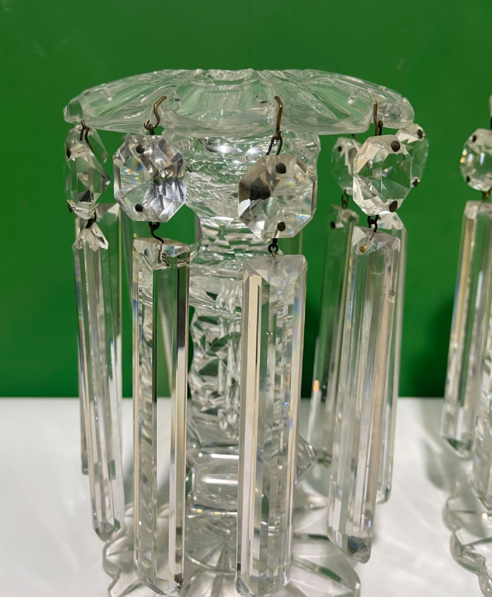 A pair of clear cut glass table lustres featuring faceted stems, starburst cut bases, and hanging crystal prism drops suspended from wire hooks. View IV